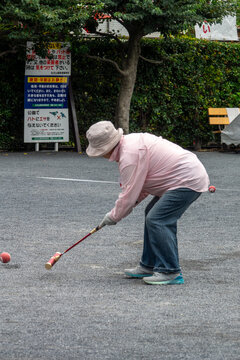 Elderly woman hitting a ball with a mallet during a gateball game, Kanto region, Tokyo, Japan