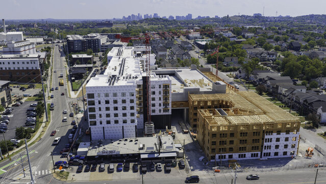 Aerial view of a large building complex under construction featuring wooden framing, white protective wrap, and red cranes in an urban setting in Nashville, TN, United States.