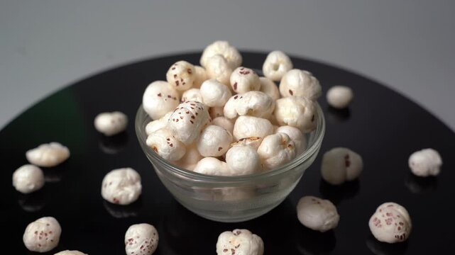 Fresh fox nuts, Euryale ferox, pop into a glass bowl on a dark table surface in a studio setting for a healthy snack video project