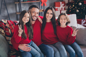 Naklejka premium Happy family in matching red sweaters sitting on a couch celebrating Christmas at home with smiling children and wrapped gifts