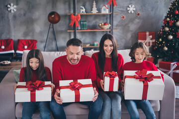 Naklejka premium Family opening Christmas gifts together on couch at home, parents and children wearing red sweaters celebrating holiday joy