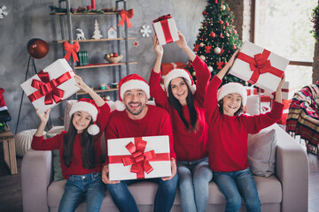 Naklejka premium Happy family wearing Santa hats opening Christmas gifts together on couch in decorated living room