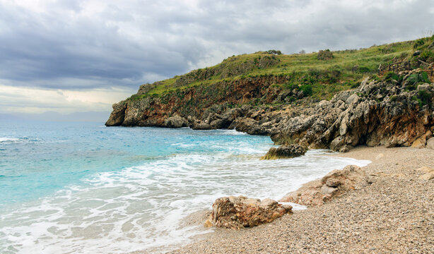Dramatic cliff shoreline with tranquil turquoise sea and distant mountains under cloudy sky
