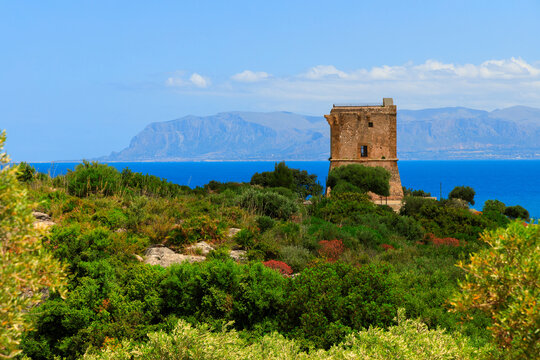 Ancient stone watchtower perched on a verdant hill overlooking the sparkling blue sea