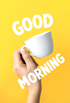 Cheerful good morning greeting with a hand holding a white coffee cup on yellow background