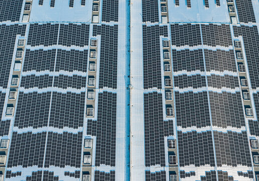 Aerial view of a massive industrial rooftop covered with a geometric pattern of photovoltaic solar panels and renewable energy infrastructure in Valence, Auvergne-Rhone-Alpes, France.