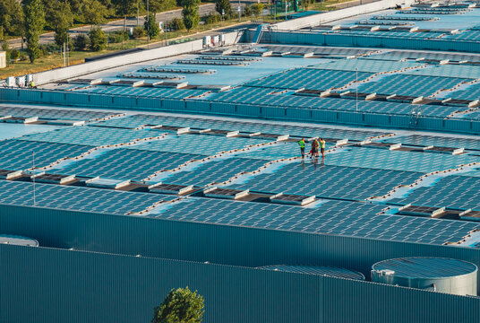 Aerial view of workers inspecting solar panels on an industrial warehouse rooftop, highlighting photovoltaic maintenance and renewable energy in Valence, Auvergne-Rhone-Alpes, France.