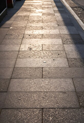 Obraz premium Urban commute and city travel, empty sidewalk with golden hour sunlight and long shadows on stone pavement in a modern metropolitan environment