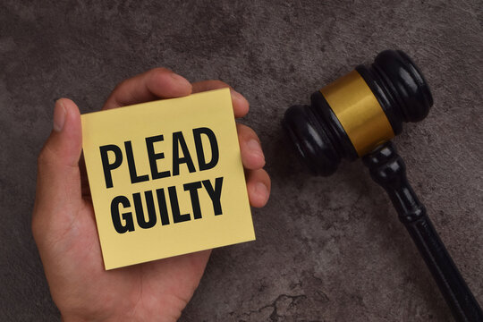 Hand holding a note labeled plead guilty beside a judge's gavel, symbolizing criminal charges, court proceedings, legal responsibility, and admission of guilt.