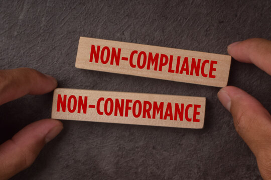 Wooden blocks labeled non-compliance and non-conformance, representing regulatory failure, quality issues, standards violations, risk management, and corrective action.