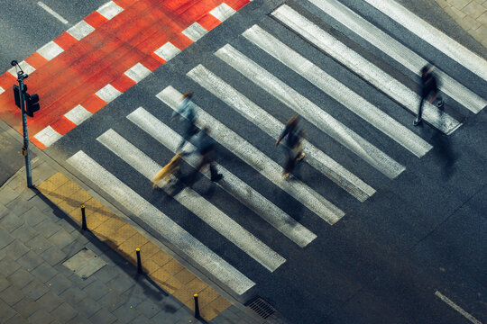 Aerial view of blurred pedestrians walking across a white-striped crosswalk on an asphalt road with red markings in Poland.