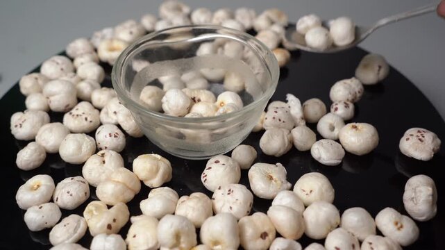 Healthy fox nut snack Euryale ferox preparation on black surface with bowl and spoon for nutrition and diet concept