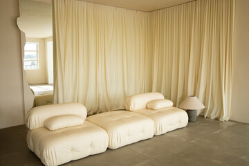 Minimalist interior design background closeup with modern cozy cream modular sofa armchair, elegant beige curtains texture and wave mirror, luxury scandinavian home decor horizontal copy space.