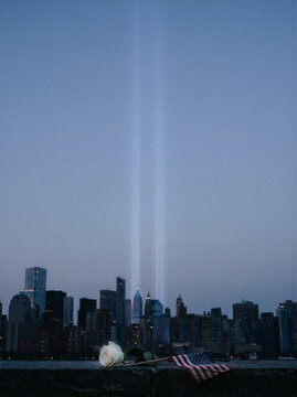 9/11 Memorial Tribute New York City Skyline, Twin Beams Of Light And Single White Rose Beside American Flag To Commemorate September 11 Patriot Day Anniversary In Manhattan Evening Urban, Remembrance