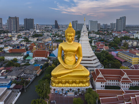 Aerial view of the massive golden Buddha statue at Wat Paknam Phasi Charoen, surrounded by traditional temple buildings and the urban cityscape of Bangkok, Krung Thep Maha Nakhon, Thailand.