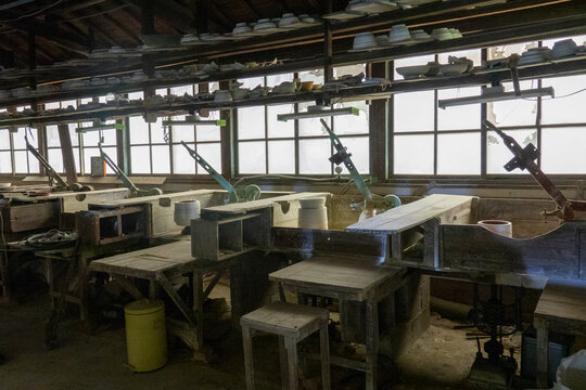 Wide interior view of a pottery workshop with workbenches trimming machines and factory windows, Kyushu region, Arita, Japan