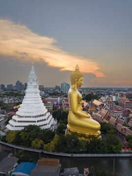 Aerial view of the giant golden Buddha statue and white stupa at Wat Paknam Phasi Charoen, surrounded by temple buildings and urban cityscape in Bangkok, Krung Thep Maha Nakhon, Thailand.
