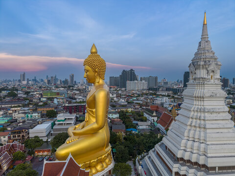 Aerial view of the giant golden Buddha statue and white stupa at Wat Paknam Phasi Charoen overlooking the urban skyline of Bangkok, Krung Thep Maha Nakhon, Thailand.