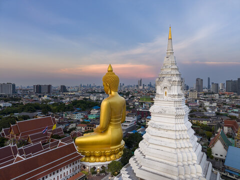 Aerial view of the giant golden Buddha statue and white stupa at Wat Paknam Phasi Charoen overlooking the Bangkok skyline at sunset in Bangkok, Krung Thep Maha Nakhon, Thailand.