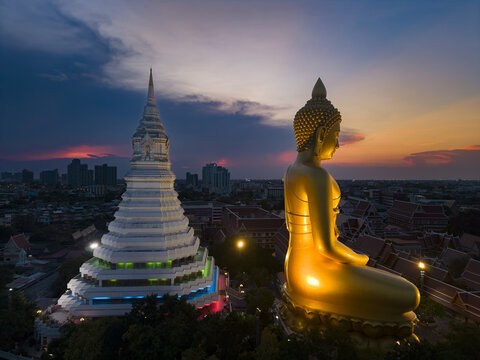 Aerial view of the giant golden Buddha statue and white stupa at Wat Paknam Phasi Charoen during sunset in Bangkok, Krung Thep Maha Nakho, Thailand.