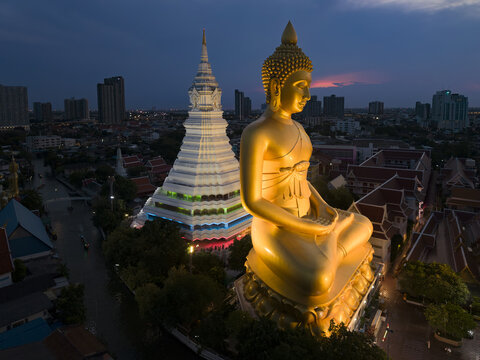 Aerial view of the giant golden Buddha statue and the illuminated white stupa at Wat Paknam Phasi Charoen at twilight in Bangkok, Krung Thep Maha Nakho, Thailand.