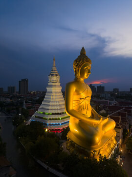 Aerial view of the giant golden Buddha statue and the white stupa of Wat Paknam Phasi Charoen illuminated at twilight in Bangkok, Krung Thep Maha Nakho, Thailand.