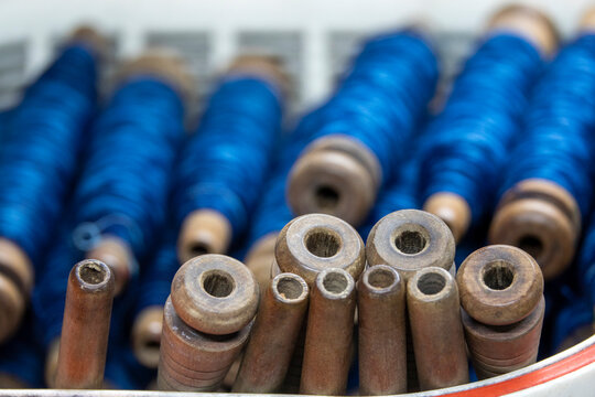Close-up of indigo blue thread spools standing upright beside empty wooden bobbin tubes, Kyushu region, Chikugo, Japan
