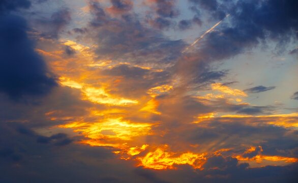 Dramatic burning sunset clouds in heaven with golden rays of light and fluffy colorful clouds, heavenly sky background