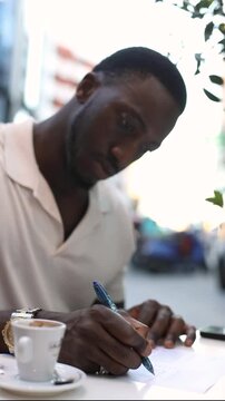 Close-up of man writing on document outdoors with coffee. Close-up of a man writing with a ballpoint pen on a document outdoors beside a cup of coffee.