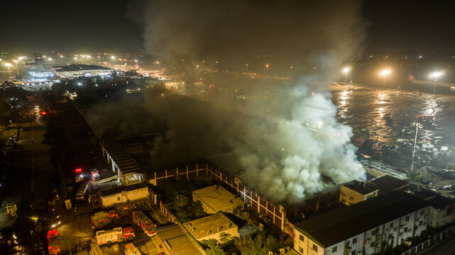 Aerial view of a large fire burning at an airport facility at night, with thick smoke rising into the air and emergency vehicles responding on the ground in Dhaka, Dhaka Division, Bangladesh.
