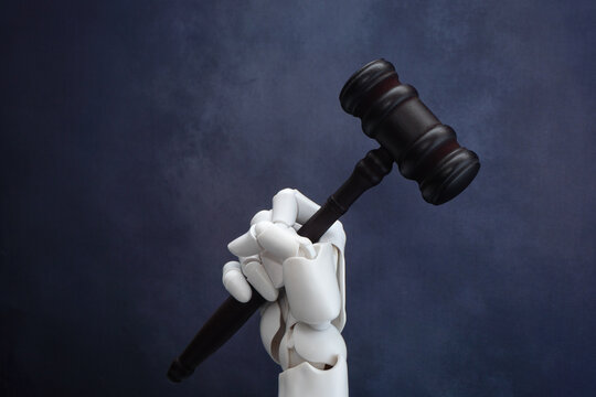 White robotic hand holding a dark wooden judge gavel. Artificial intelligence in law, automated court decisions concept.