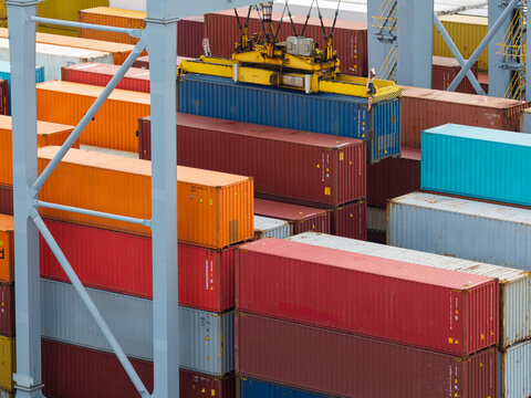 Aerial view of colorful shipping containers being stacked by a large industrial crane at a busy port in the United Kingdom.