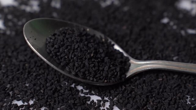 Black cumin seeds or Nigella sativa on a metal spoon over a pile of spice, macro close up shot for healthy food and cooking video