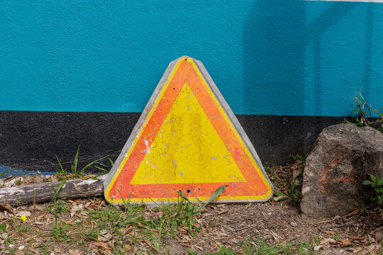 Weathered triangular warning sign leaning against blue wall