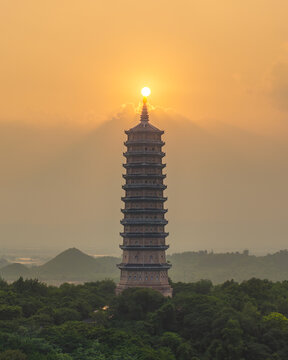 Aerial view of Bao Thien Stupa illuminated by the golden sunset light, surrounded by lush greenery in Tay Hoa Lu, Ninh Binh, Vietnam.