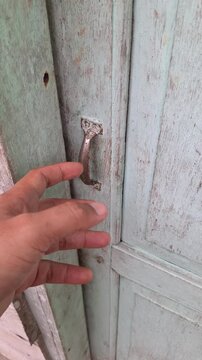 Hesitant hand reaching to open an old rustic wooden door with a vintage handle for suspense, mystery, and thriller concept