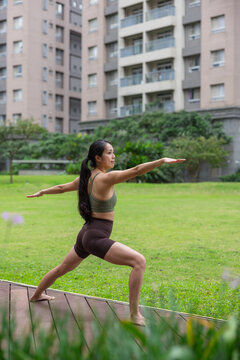 Woman practicing warrior two yoga pose on grass outdoors