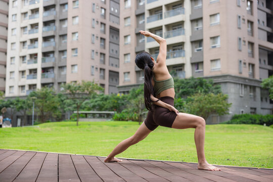 Woman doing reverse warrior yoga pose on park lawn