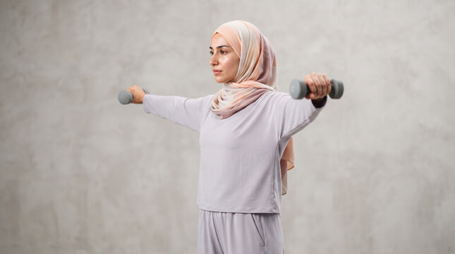 Woman in hijab doing lateral raises with dumbbells