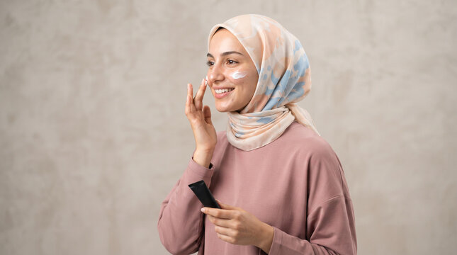 Muslim woman in hijab applying face cream from tube