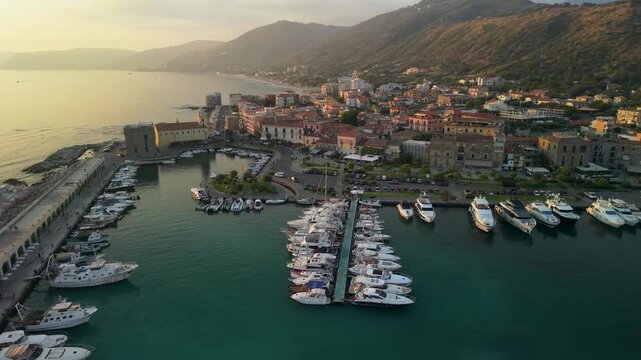Acciaroli Cilento Italy 4K cinematic drone video. Golden hour sunset orbit over harbor with medieval tower church and yachts. Authentic Mediterranean travel b roll stock footage