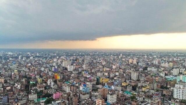 Aerial view of the dense urban landscape of Dhaka featuring a vast expanse of residential buildings and high-rise structures under a dramatic cloudy sky in Dhaka, Dhaka Division, Bangladesh.