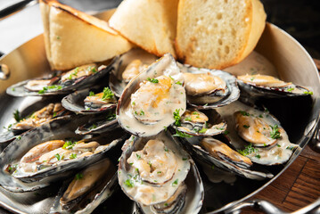 Steaming pan of fresh cooked mussels in creamy garlic sauce, served with slices of crusty bread. © pavel siamionov