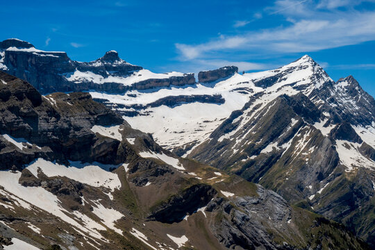 Rugged mountain peaks with lingering snowfields rise beneath a deep blue summer sky in Ordesa y Monte Perdido National Park, Spanish Pyrenees.