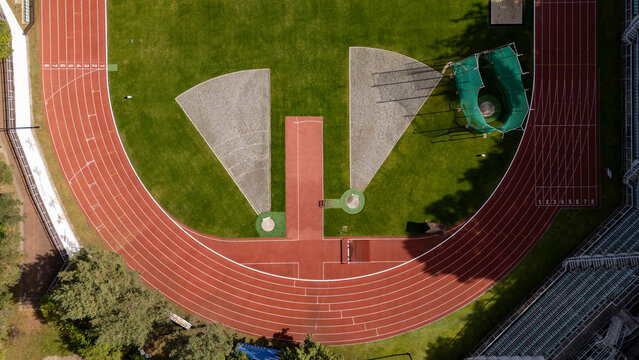 Aerial view of a running track and field facility with a red synthetic surface, green grass infield, and throwing sectors in Gdansk, Poland.