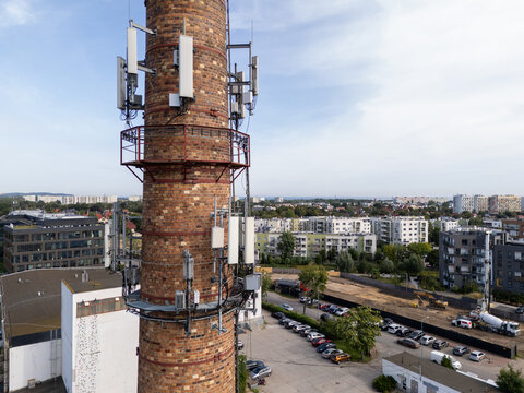 Aerial view of an old brick chimney repurposed as a telecommunications tower with multiple antennas, surrounded by modern residential buildings and a parking lot in Gdansk, Poland.