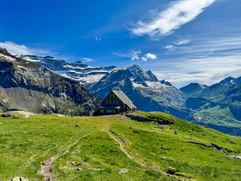 Mountain trail crosses a bright green alpine meadow with sweeping Pyrenean peaks in Ordesa y Monte Perdido National Park, Spain.