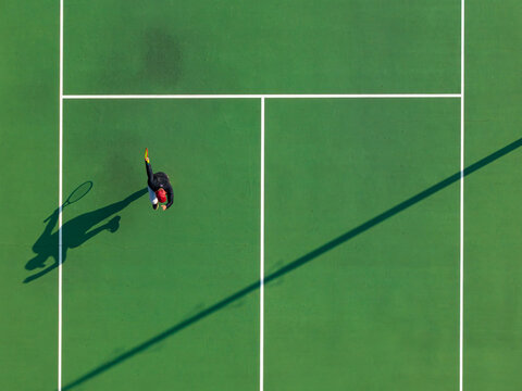 Aerial view of a tennis player celebrating point with a dance on a green court with long shadows in Kecamatan Prambanan, Jawa Tengah, Indonesia.