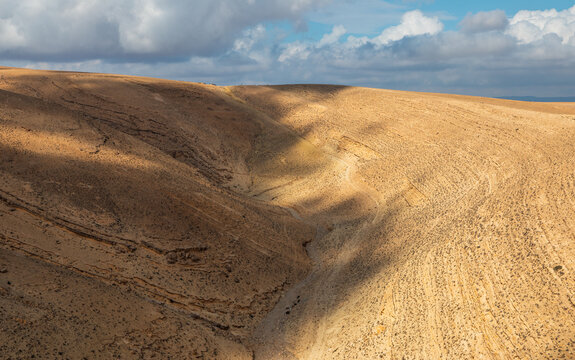 Aerial view of the rugged desert landscape near Shobak, featuring deep valleys, rocky terrain, and dramatic cloud shadows cast over the arid hills in Shobak, Ma'an Governorate, Jordan.