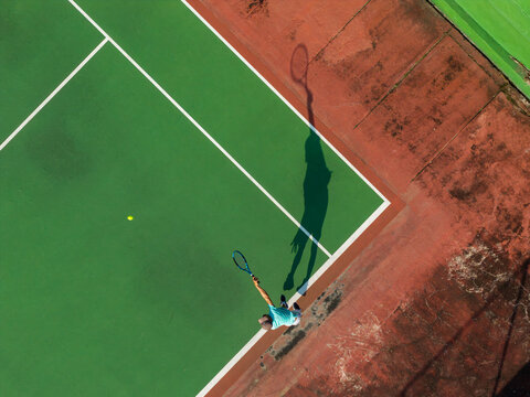 Aerial view of a tennis player performing a serve on a green court with a red border in Kecamatan Prambanan, Jawa Tengah, Indonesia.